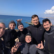 Load image into Gallery viewer, Group of people in wetsuits posing for a selfie by the ocean.

