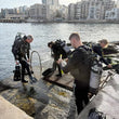 Load image into Gallery viewer, Four divers standing by the shore on our house reef in Bugibba, getting kitted up and ready for a dive with the sea in the background
