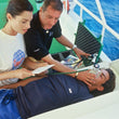 Load image into Gallery viewer, Person receiving oxygen therapy on a boat with a medical professional and another person assisting.
