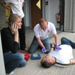 Load image into Gallery viewer, Person performing CPR on a mannequin while others observe, with a focus on emergency response.
