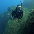 Load image into Gallery viewer, A scuba diver demonstrating good trim and buoyancy control while exploring underwater rocky terrain
