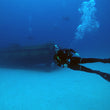Load image into Gallery viewer, A diver poses in front of the P29 wreck at Cirkewwa, Malta, in crystal-clear blue water
