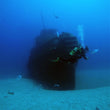 Load image into Gallery viewer, A diver swims around the bow of the Tugboat Rozi on a deep pleasure dive in Cirkewwa, Malta, using a clearly-labelled nitrox cylinder for extended bottom time
